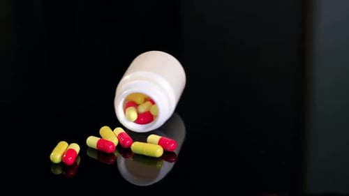 Pills Spilling from Plastic Container on Reflective Surface