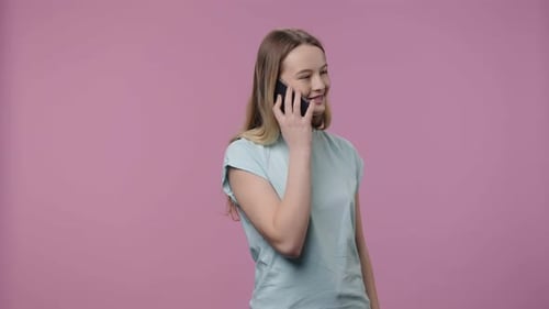 Young Woman Talking on Phone Against Pink Backdrop