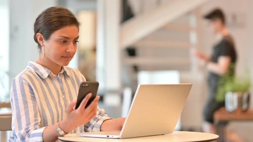 Indian Woman with Laptop Using Smartphone in Cafe