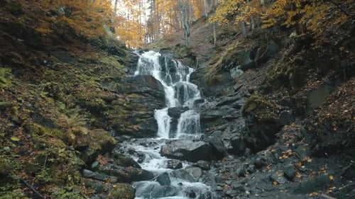 Wasserfallkaskade fließt von großen Felsen zwischen gelben Bäumen