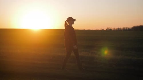 Female Farmer in Plaid Shirt and Hat Walks Through the Field. A Worker Go with His Rubber Boots at