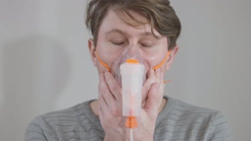 Gros plan d'un homme brun de race blanche malade aux yeux gris prenant des médicaments à l'aide d'un nébuliseur