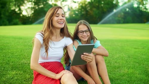 Mother and Daughter Laughing in Park. Woman and Girl Talking at Camera on Tablet