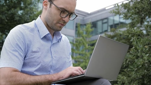 Cheerful Man Working on a Laptop Computer Outside Office