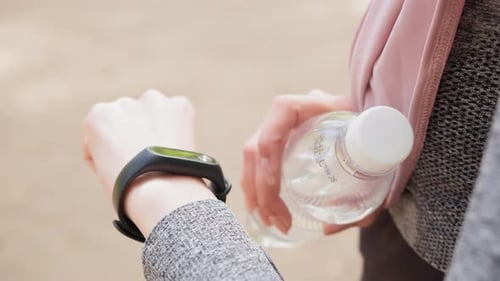 Woman Checks Fitness Tracker Holding Water Bottle