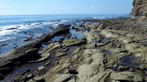 Tracking shot of a young man running on a rocky ocean beach shoreline