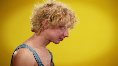 Side View Closeup of Young Queer Man Standing at Yellow Background on the Left Putting Red Flower in