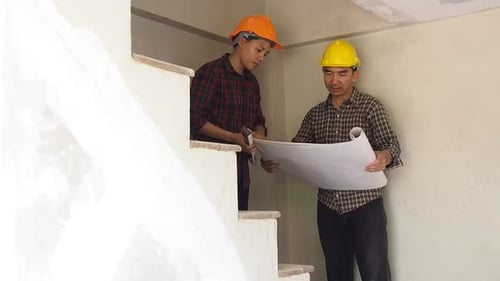 Construction Workers Review Blueprints on Building Site