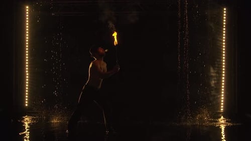 The Fakir Breathes Fire in a Dark Studio in the Rain. A Silhouette of a Half Naked Man