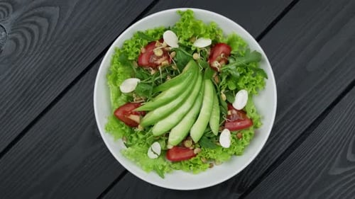 Delicious Salad with Avocado Arugula and Tomatoes on Black Wooden Table Top View
