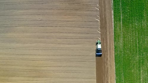 Blue tractor working on spring field, aerial view