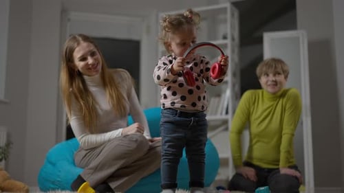 Little Girl Plays with Headphones Watched by Adults