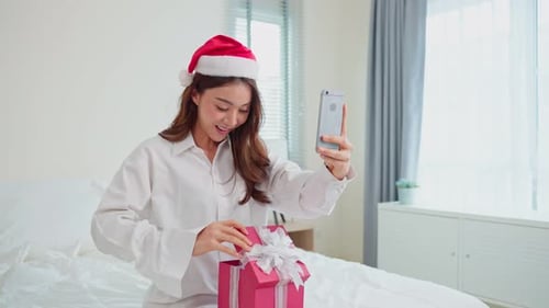 Woman in Santa Hat Opening Gift on Bed