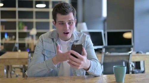 Sad Male Designer Facing Loss on Smartphone in Office