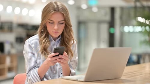 Businesswoman with Laptop Using Smartphone in Office