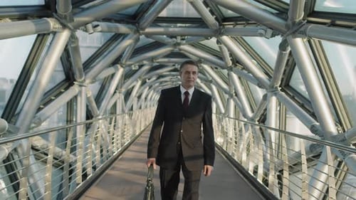 Middle-Aged Business Man Walking Along Glass Bridge