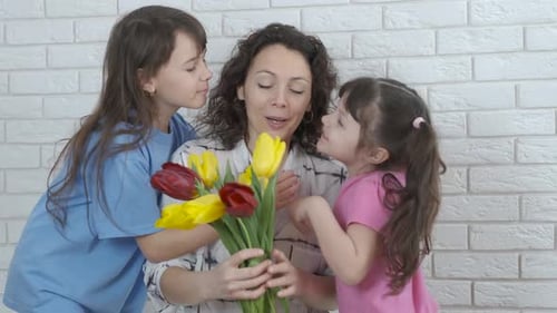 Two Children Give Flowers to Their Happy Mother