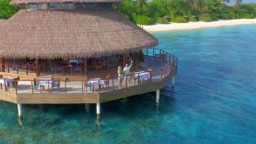 Aerial View on Young Couple in Water Restaurant on the Beach in Maldives Resort Island