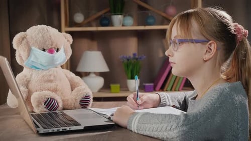 School Online Pupil Doing Lessons Near Laptop Next to a Teddy Bear in a Protective Mask
