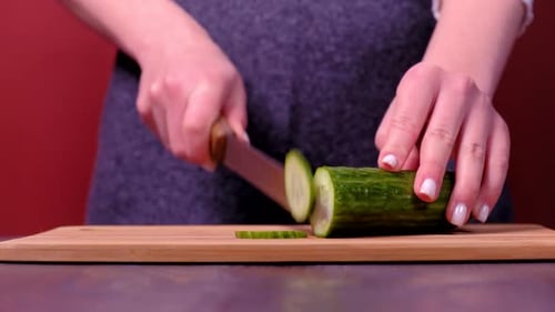 Woman Slices Cucumber on Cutting Board in Kitchen