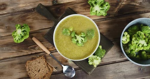 Bowl of broccoli soup with bread on wood table