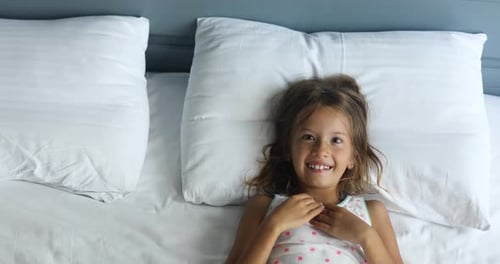 Happy Girl Smiling in Bed Underneath White Sheets