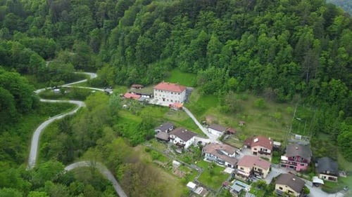 Flying toward a small settlement with old big house at the top of the hill beside green forest.