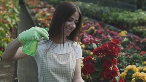 Girl sprays flowers in the garden. Caucasian woman takes care of plants by moisturizing them. Slow m