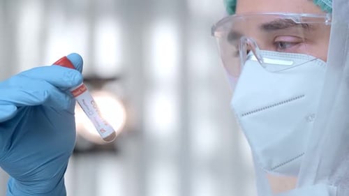 Doctor in Hazmat Suit and Protective Mask Holds a Test Tube with COVID19 Virus