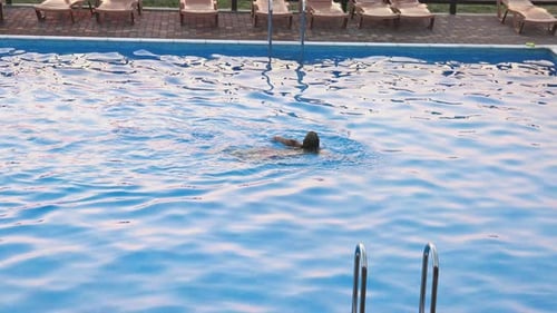Woman Swims in a Pool with Clear Water on the Background of a Summer Sunset on Vacation