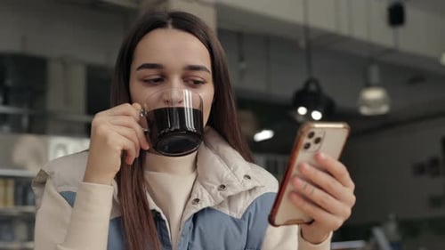Woman Using Smartphone While Drinking Coffee at Cafe