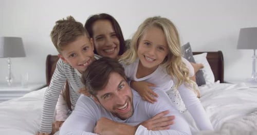 Smiling Family Pile on Bed Together at Home