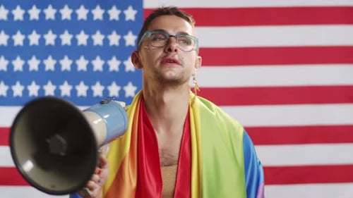 Young Adult Speaks with Megaphone in Front of Flag