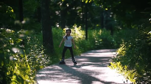 A Little Girl in Helmet Skating in the Forest on Her Rollers