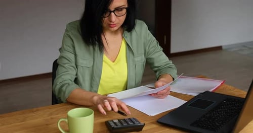 Woman Works with Papers and Calculator at Home