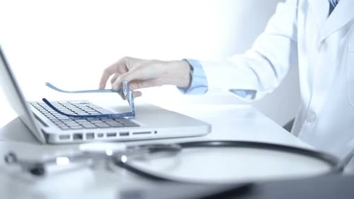 Medical Professional Using Laptop and Putting on Glasses