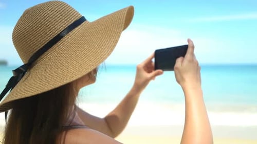 Young Traveler Woman in Hat Taking Photo on Smartphone in Ocean Beach