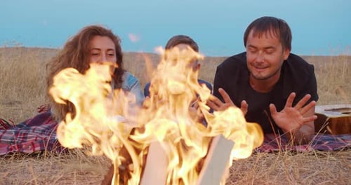Family Sitting in the Evening Round a Bright Bonfire Outdoors