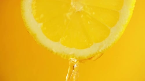Lemon Slice with Dripping Juice on Yellow Background