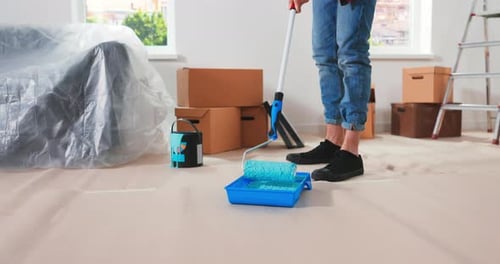 Kaukasischer Mann bereitet sich auf Reparaturen in neuer Wohnung vor und setzt Walze in Container mit Grün