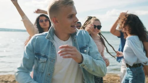 Ralenti d'un bel homme blond dansant avec des amis lors d'une fête en plein air sur la plage