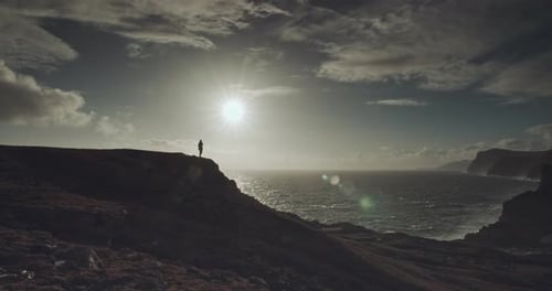Lone Figure on Cliff Overlooking Dramatic Ocean Landscape