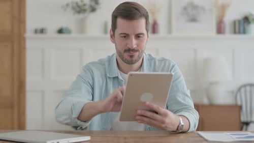 Young Man Celebrating Success on Tablet in Office