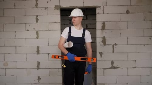 Un constructor masculino con herramientas y dibujos en sus manos en una casa inacabada