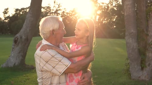 Grandfather Embracing Granddaughter at Sunset in Park
