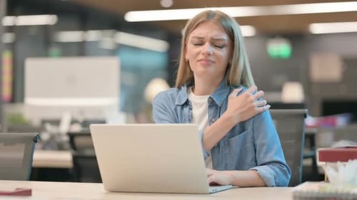Woman with shoulder pain works on laptop in office