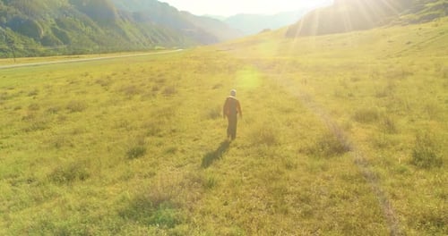 Flight Over Backpack Hiking Tourist Walking Across Green Mountain Field. Huge Rural Valley at Summer