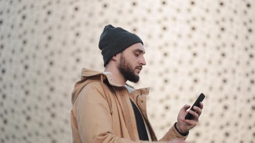 Happy Young Beard Man Using Smartphone Walking in the Street Near Shopping Mall. He Is Wearing an