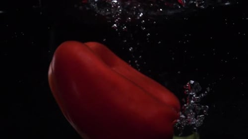 Rote Paprika fällt ins Wasser. Zeitlupe. Schwarzer Hintergrund. Video zum Thema Essen