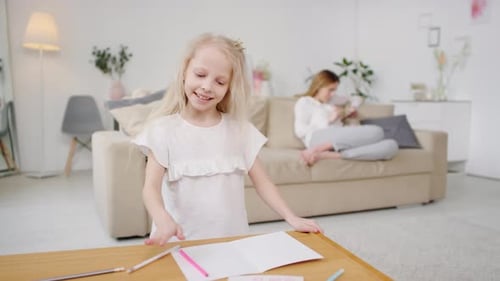 Child Drawing at Table While Other Sibling Relaxes